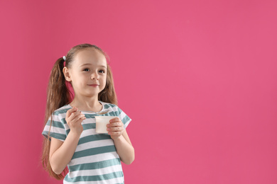 Photo of Cute little girl with tasty yogurt on pink background. Space for text