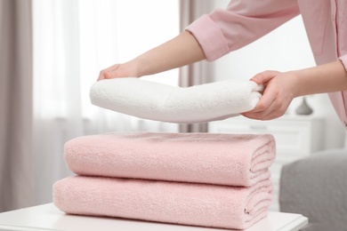 Photo of Woman stacking clean towels on table in room