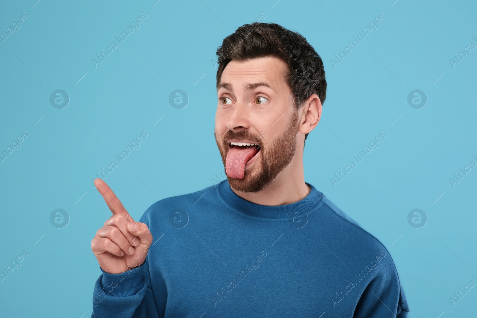 Photo of Man showing his tongue and pointing at something on light blue background