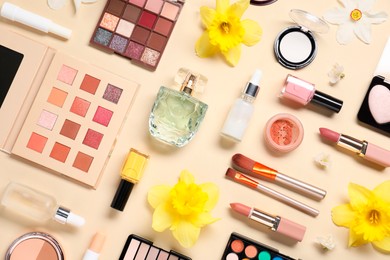 Photo of Flat lay composition with different makeup products and beautiful spring flowers on beige background