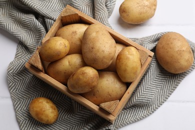 Photo of Raw fresh potatoes and wooden crate on white tiled table, top view
