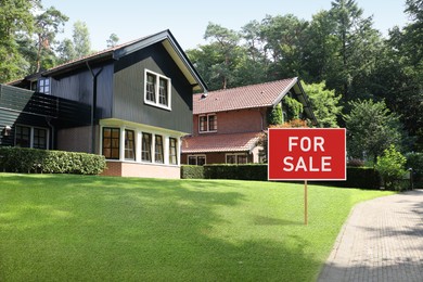 Sale sign near beautiful house outdoors. Red signboard with words