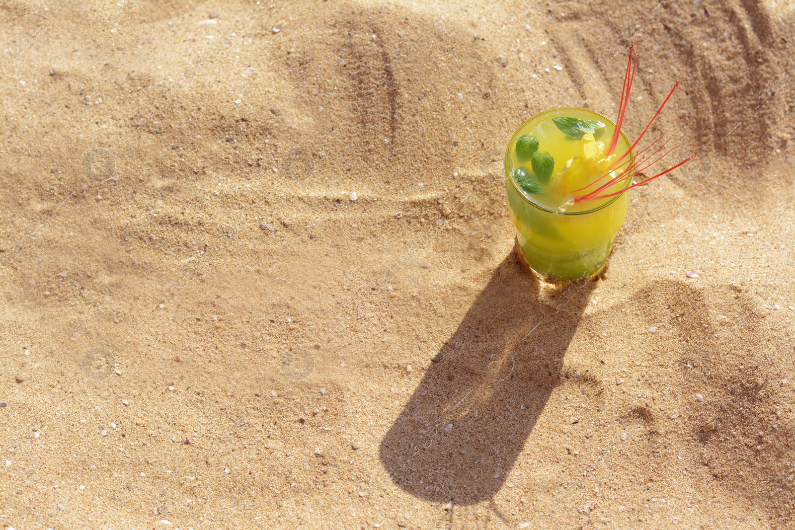 Photo of Glass of refreshing drink on sand. Space for text