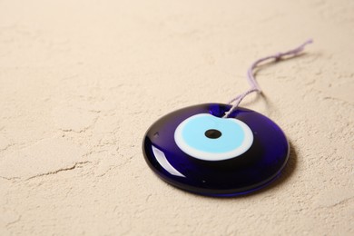 Photo of Evil eye amulet on beige textured table, closeup. Space for text