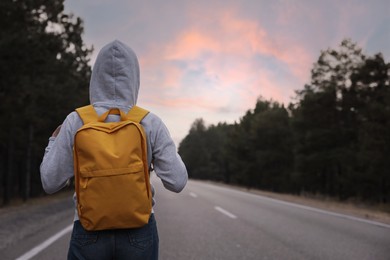 Photo of Woman with backpack on road near forest, back view