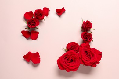 Photo of Beautiful red roses and petals on pale pink background, flat lay. Space for text