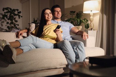 Photo of Couple watching movie with popcorn on sofa at night