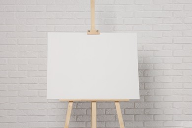 Photo of Wooden easel with blank canvas near white brick wall. Space for text