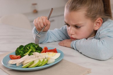 Photo of Cute little girl refusing to eat dinner in kitchen