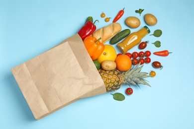 Photo of Shopping paper bag with different groceries on light blue background, flat lay
