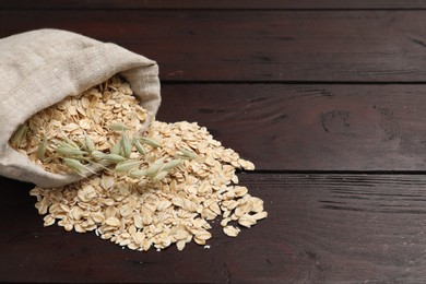 Photo of Overturned sack with oatmeal and florets on dark wooden table, space for text