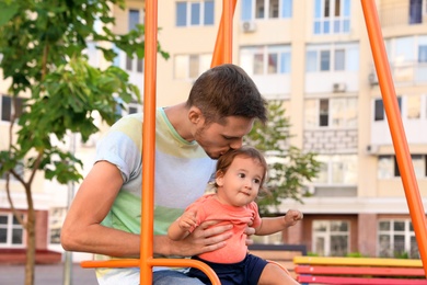 Photo of Father with adorable little baby on swing outdoors. Happy family