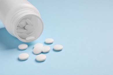 Photo of Plastic medical bottle with pills on light blue background, closeup. Space for text