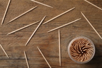 Photo of Disposable toothpicks and holder on wooden background, flat lay