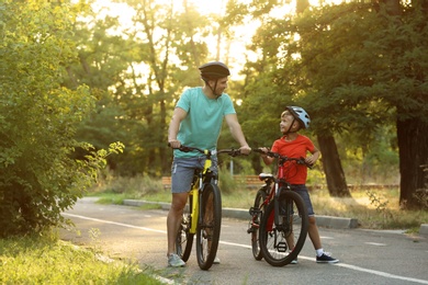 Photo of Dad and son riding bicycles in park on sunny day