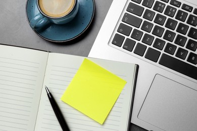 Photo of Laptop, planner, empty sticky note, pen and cup of coffee on grey table, flat lay. Space for design
