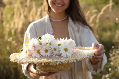 Photo of Woman holding straw hat with beautiful wild flowers outdoors, closeup