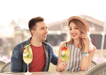 Photo of Young couple with glasses of tasty lemonade in open-air cafe