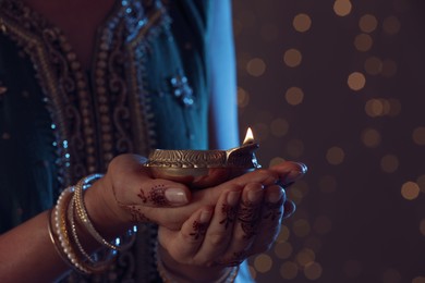 Photo of Closeup view of woman holding lit diya lamp on brown background with blurred lights, space for text. Diwali holiday