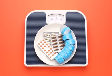 Photo of Scales with plate, weight loss pills and measuring tape on coral background, top view