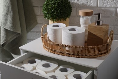 Photo of Toilet paper rolls, floral decor, dispenser and cotton pads on chest of drawers indoors