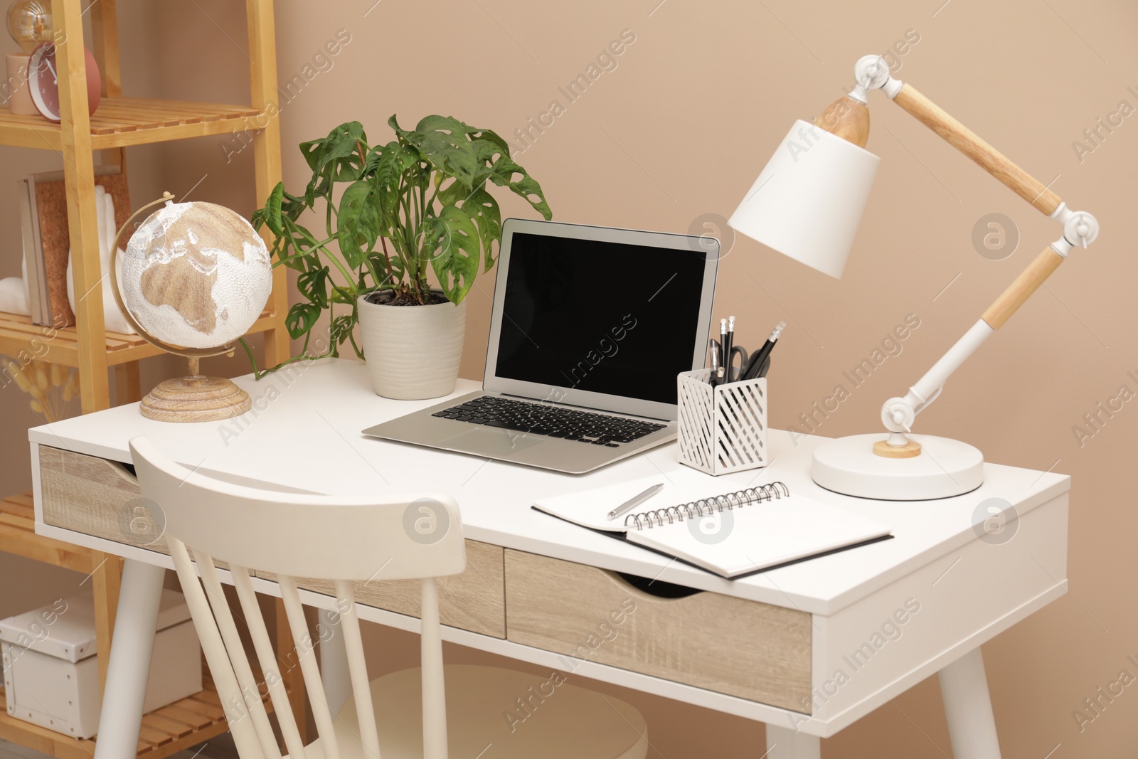 Photo of Cozy workplace with modern laptop on desk and comfortable chair at home