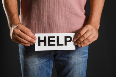Photo of Man holding paper with word HELP on black background, closeup. Urology problems