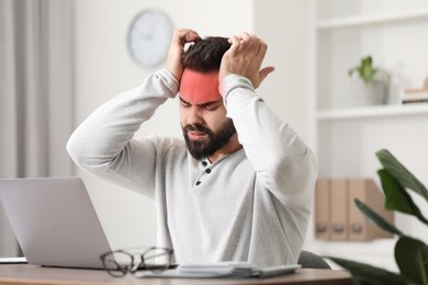 Image of Man suffering from headache at workplace indoors