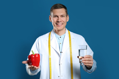 Photo of Nutritionist with glass of water and bell pepper on blue background