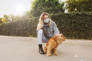 Photo of Woman in protective mask with English Cocker Spaniel outdoors. Walking dog during COVID-19 pandemic