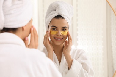 Photo of Beautiful young woman with under eye patches near mirror at home