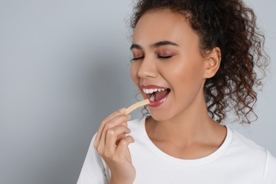 Photo of African American woman eating French fries on grey background, space for text
