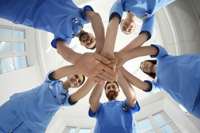Photo of Young doctors stacking hands together indoors, bottom view