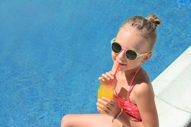 Photo of Cute little girl with glass of juice in swimming pool on sunny day. Space for text