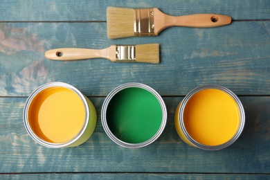 Photo of Cans with paint and brushes on wooden background, top view