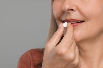 Photo of Senior woman taking pill on grey background, closeup. Space for text