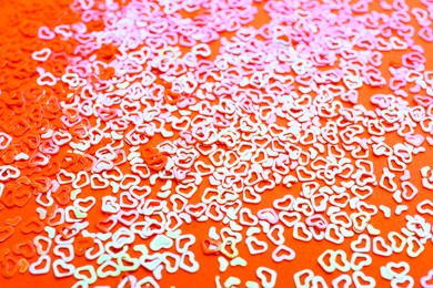 Photo of Shiny bright heart shaped glitter on coral background, closeup