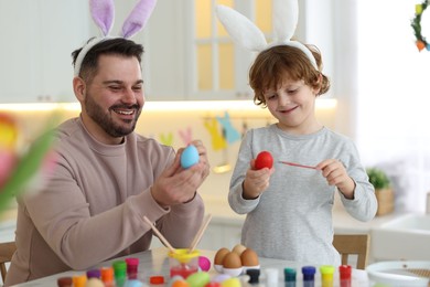 Photo of Easter celebration. Happy father with his little son painting eggs at table in kitchen