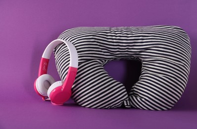 Photo of Striped travel pillow and headphones on violet background
