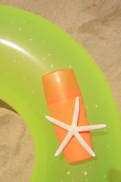 Photo of Sunscreen, starfish and inflatable ring on sand, top view. Sun protection care
