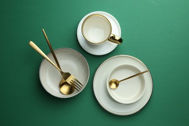 Photo of Stylish empty dishware and golden cutlery on green background, flat lay