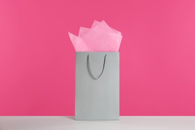 Photo of Gift bag with paper on white table against pink background