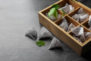 Photo of Wooden box with paper tea bags and leaves on dark grey table, space for text