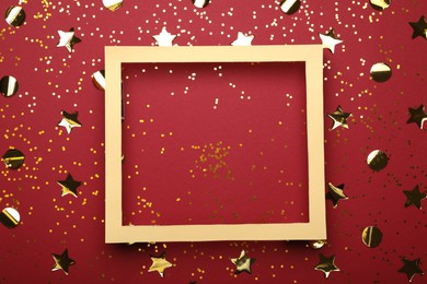 Wooden frame and confetti on red background, flat lay. Space for text