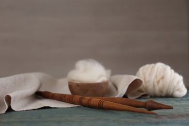 Soft white wool and spindles on blue wooden table. Space for text
