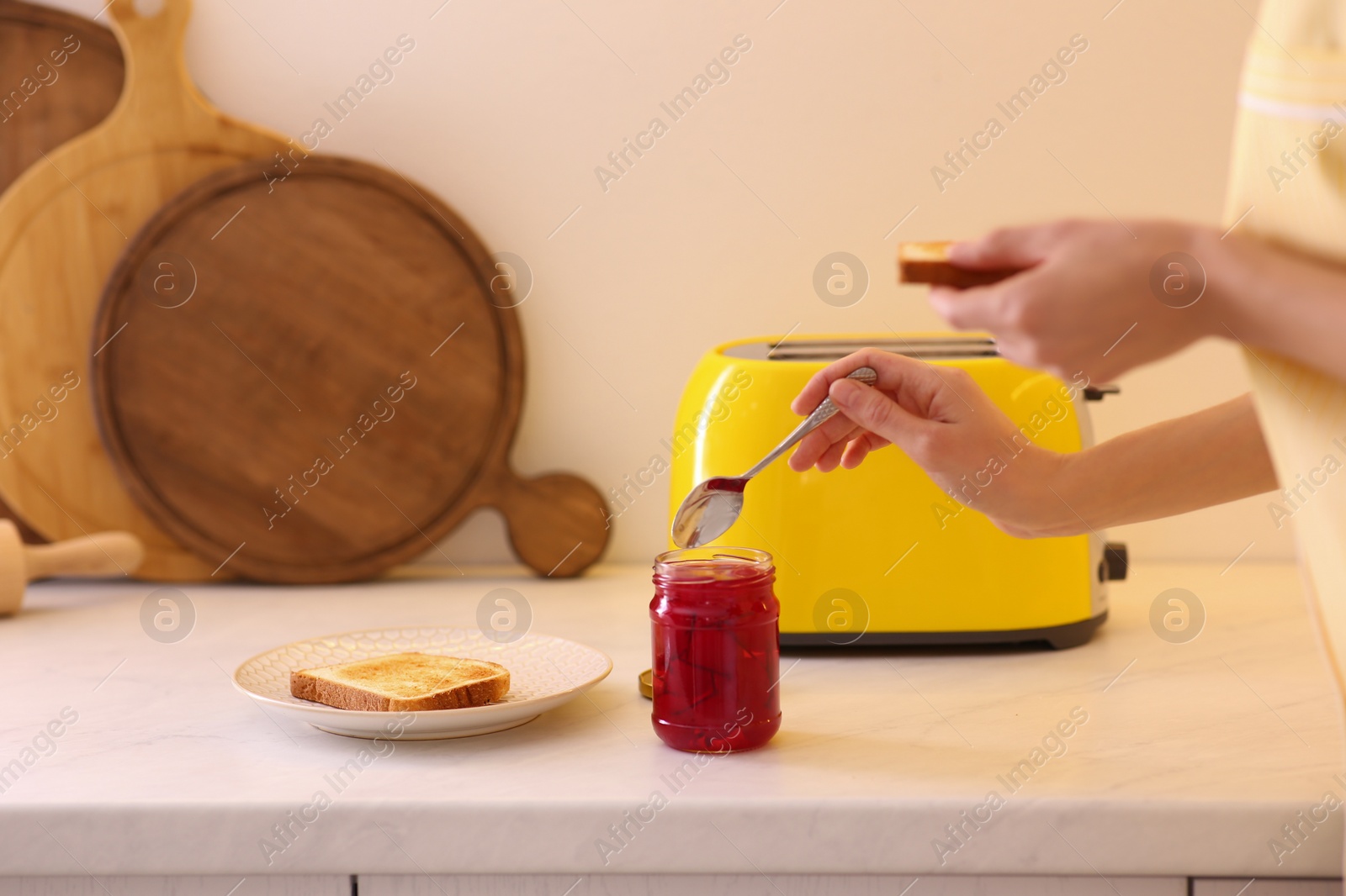 Photo of Woman making toasts with jam at table in kitchen, closeup. Weekend morning