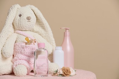 Photo of Baby cosmetic products, toy bunny and accessories on pink towel against beige background. Space for text