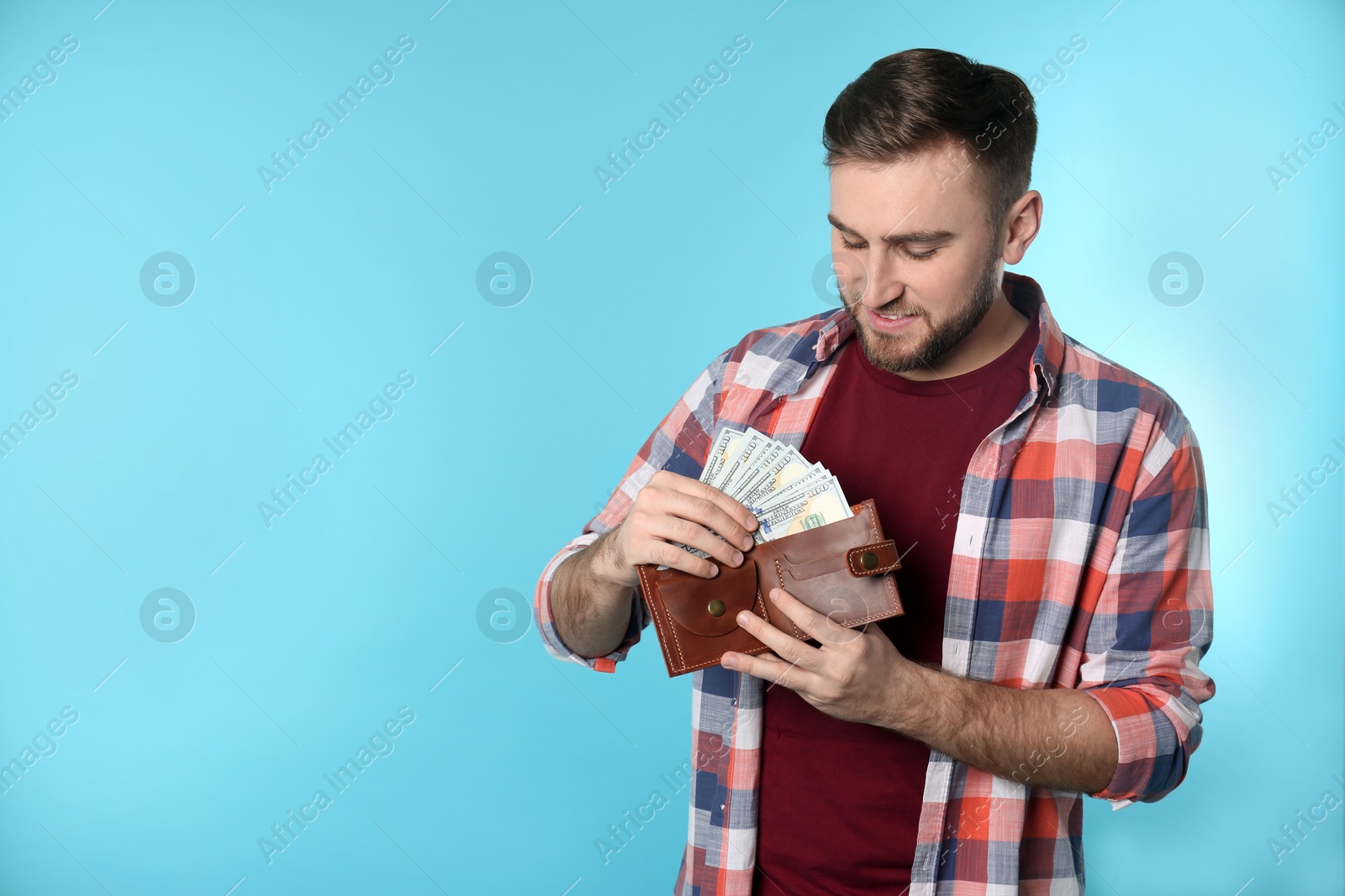 Photo of Happy young man putting money into wallet on color background. Space for text