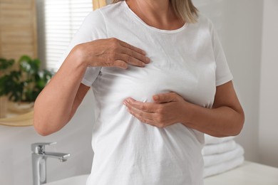 Photo of Woman doing breast self-examination in bathroom, closeup