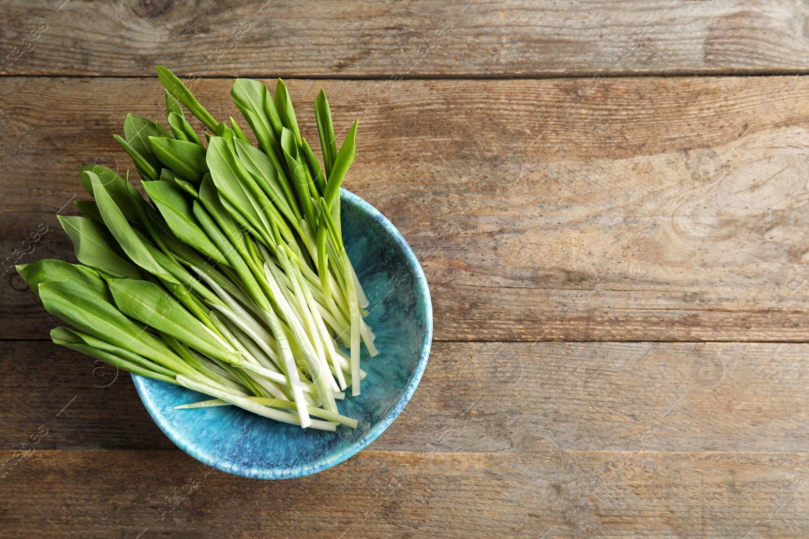 Photo of Bowl with wild garlic or ramson on wooden table, top view. Space for text